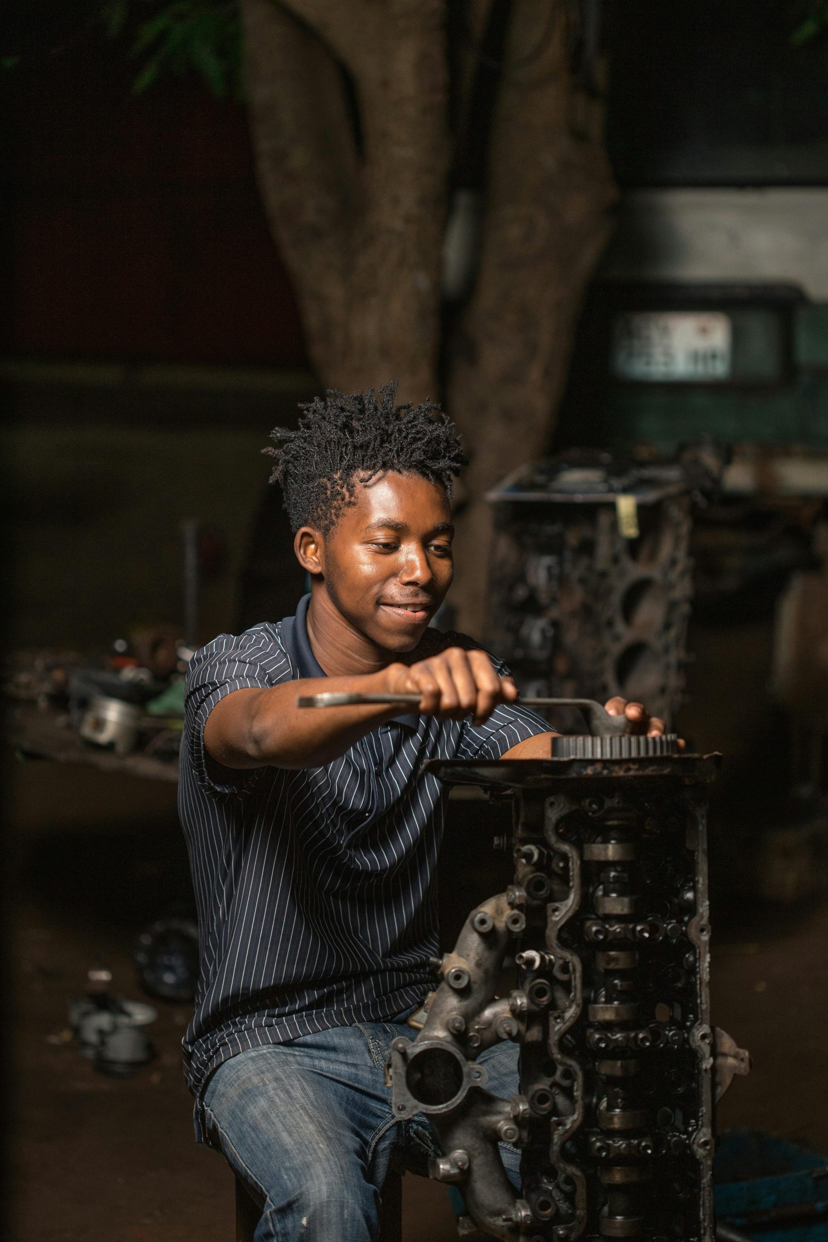 Young mechanic expertly repairs an engine in a dimly lit workshop.